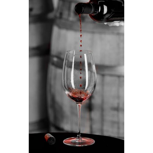 Red wine pouring into is captured in mid-air before it touches wine glass